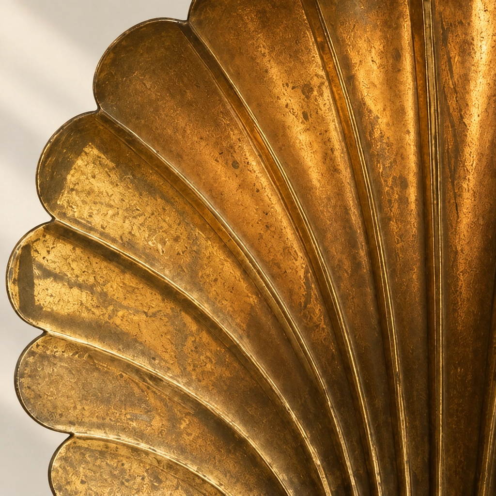 Close-up of the Solenne shell backplate, showing raised fan ridges, scalloped edge and mottled antique-brass finish