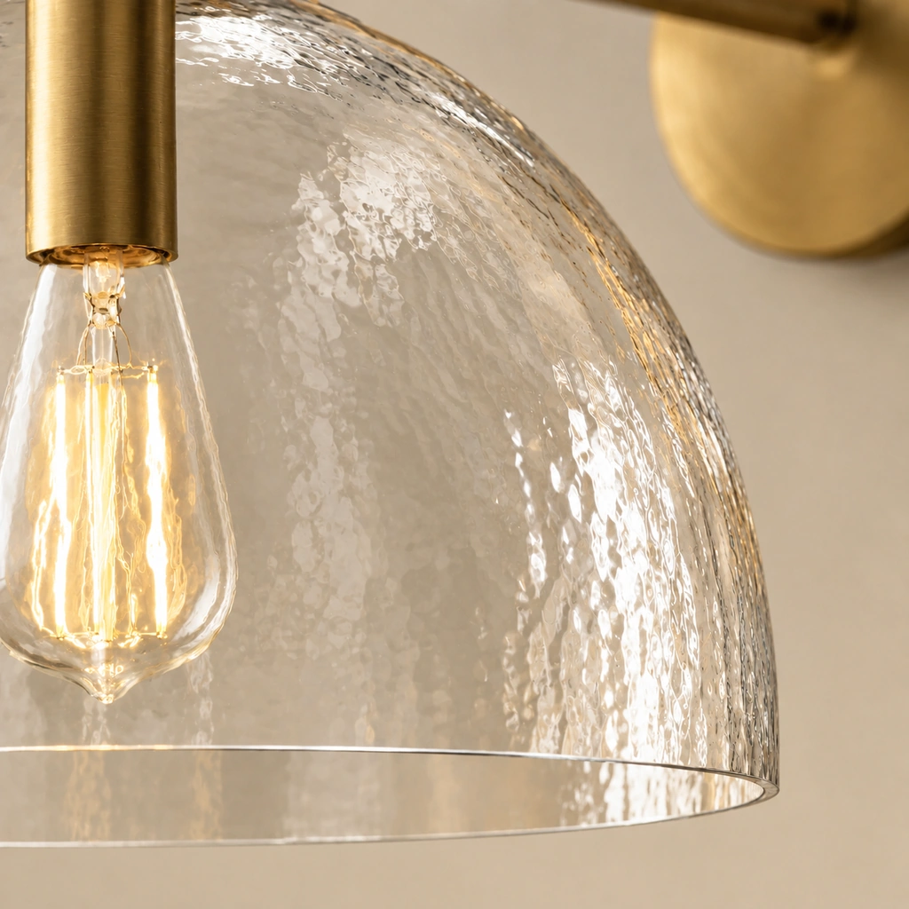 Close view of the rippled hand-blown clear glass shade with a lit filament bulb and brass socket.