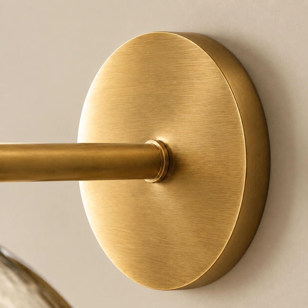 Close view of the round brushed brass wall plate with the straight arm extending from its center.