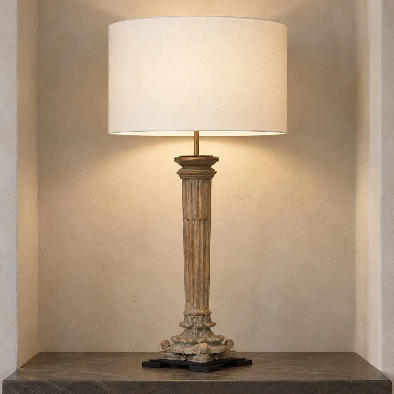 Aveline carved wood table lamp illuminated in a pale architectural alcove