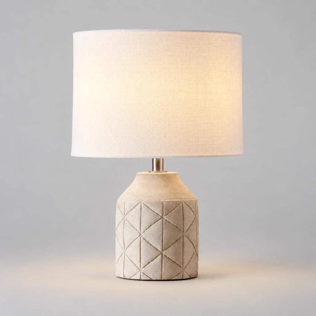 Merritt Geometric Carved Wood Table Lamp with White Drum Shade switched on in a neutral studio