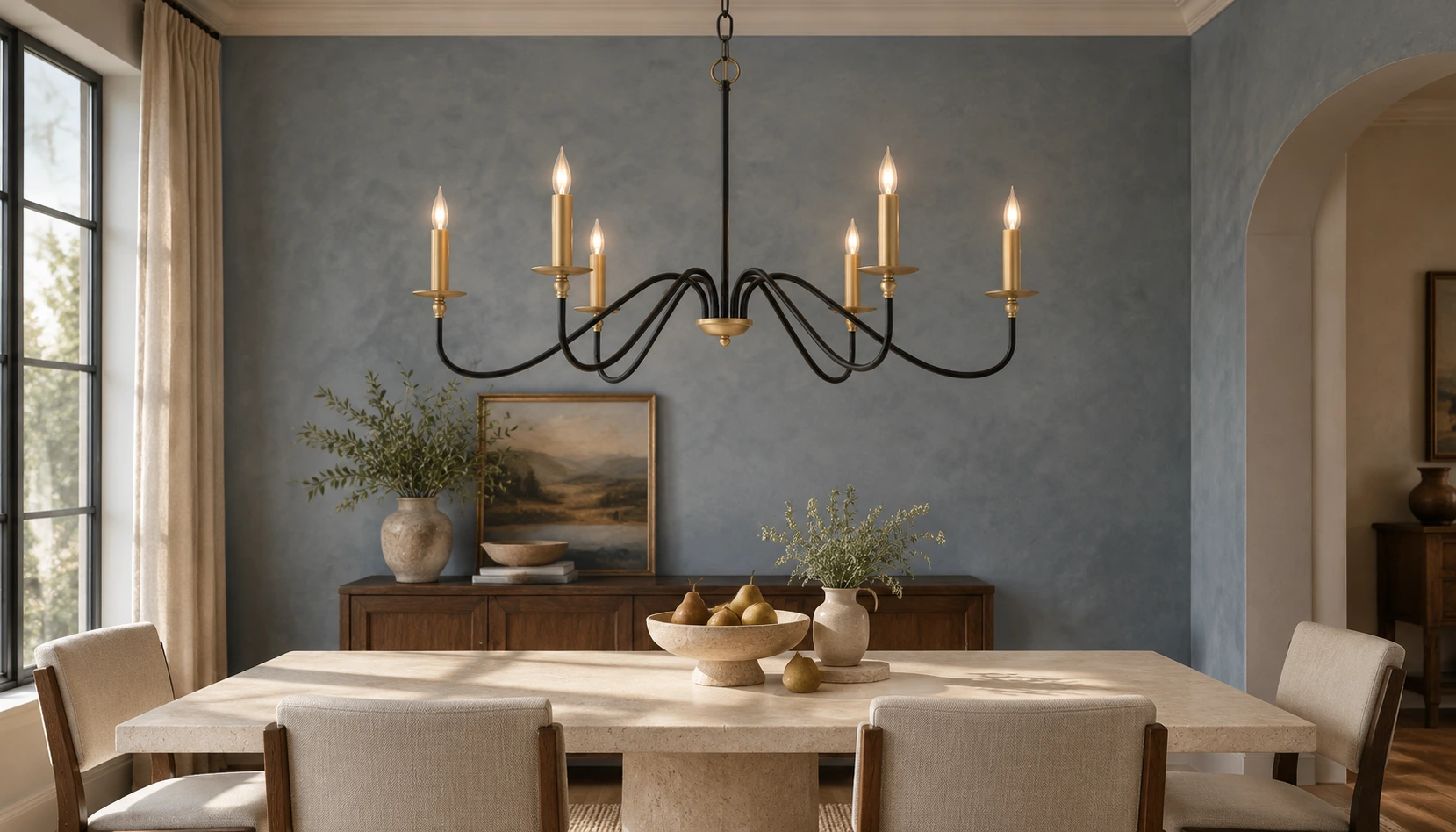 Lustre vintage Arden en fer noir illuminé au-dessus d'une table à manger en pierre calcaire pâle dans une pièce de style transitionnel bleu ardoise
