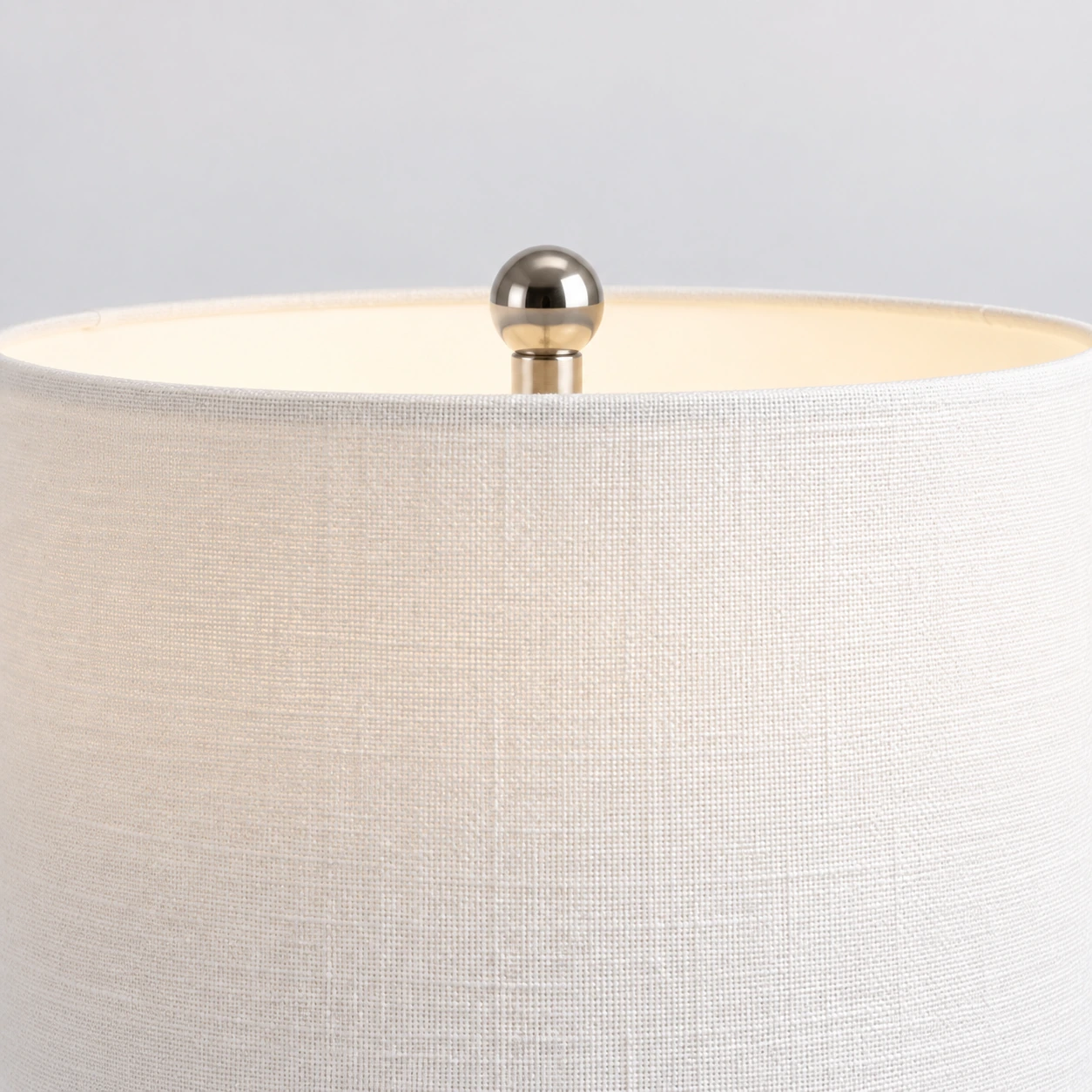 Gros plan sur l'abat-jour blanc tissé et le fleuron sphérique chromé de la lampe Odette