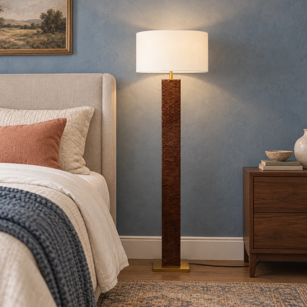 Lámpara de pie Nora de madera texturizada junto a una cama tapizada.